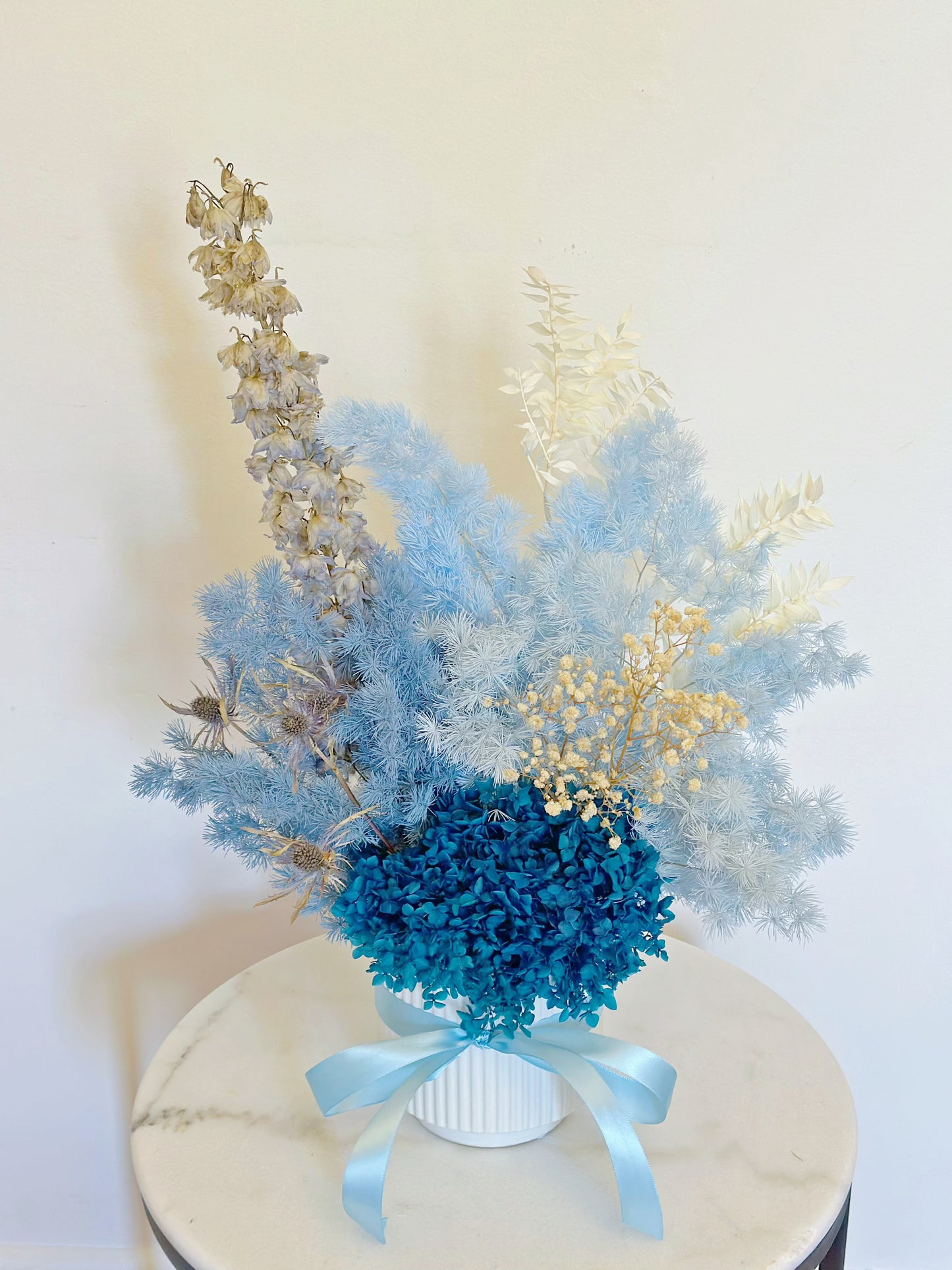 Ocean in Vase with blue preserved hydrangea and dried flowers in a white ceramic vase