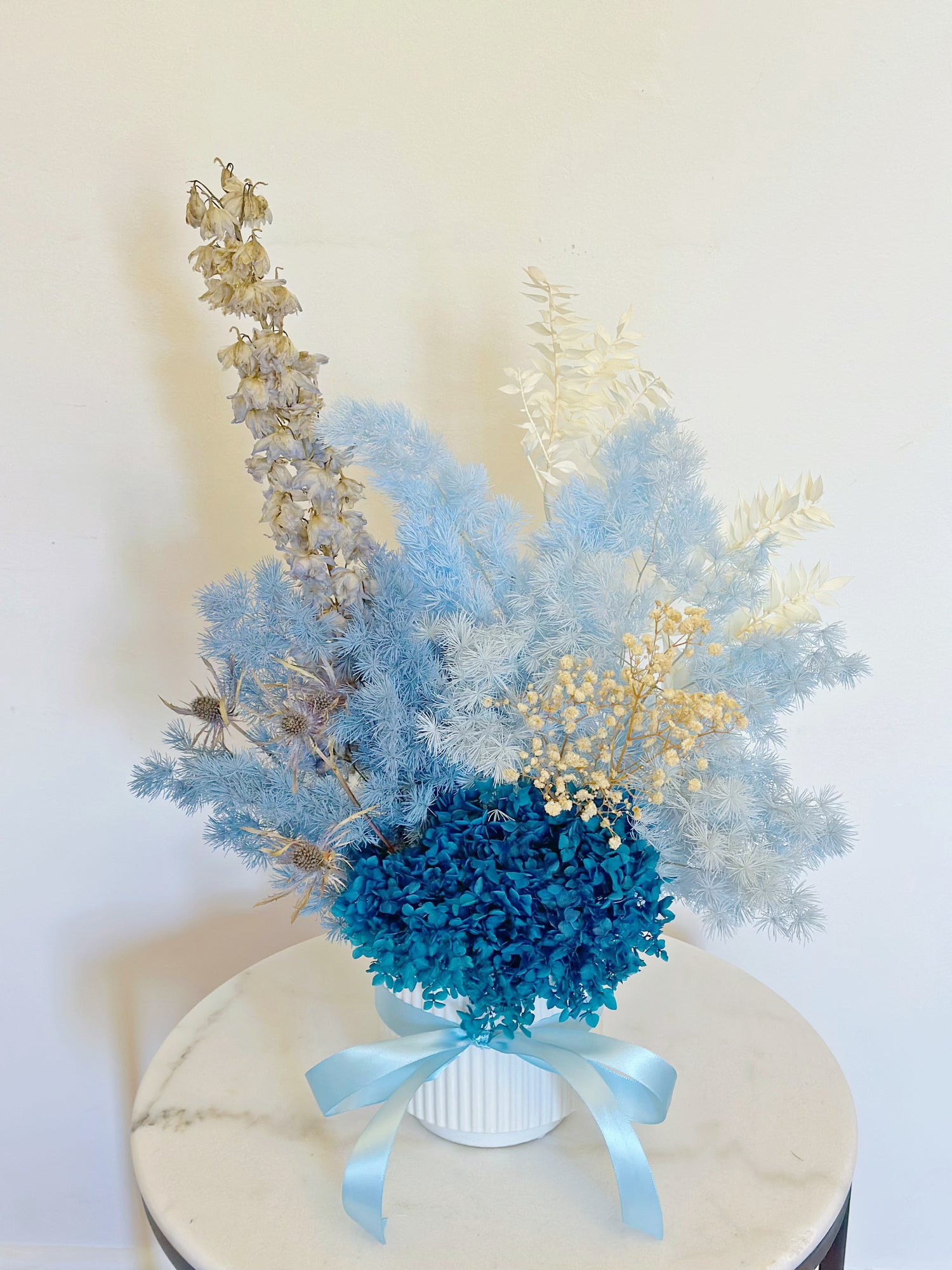 Ocean in Vase with blue preserved hydrangea and dried flowers in a white ceramic vase